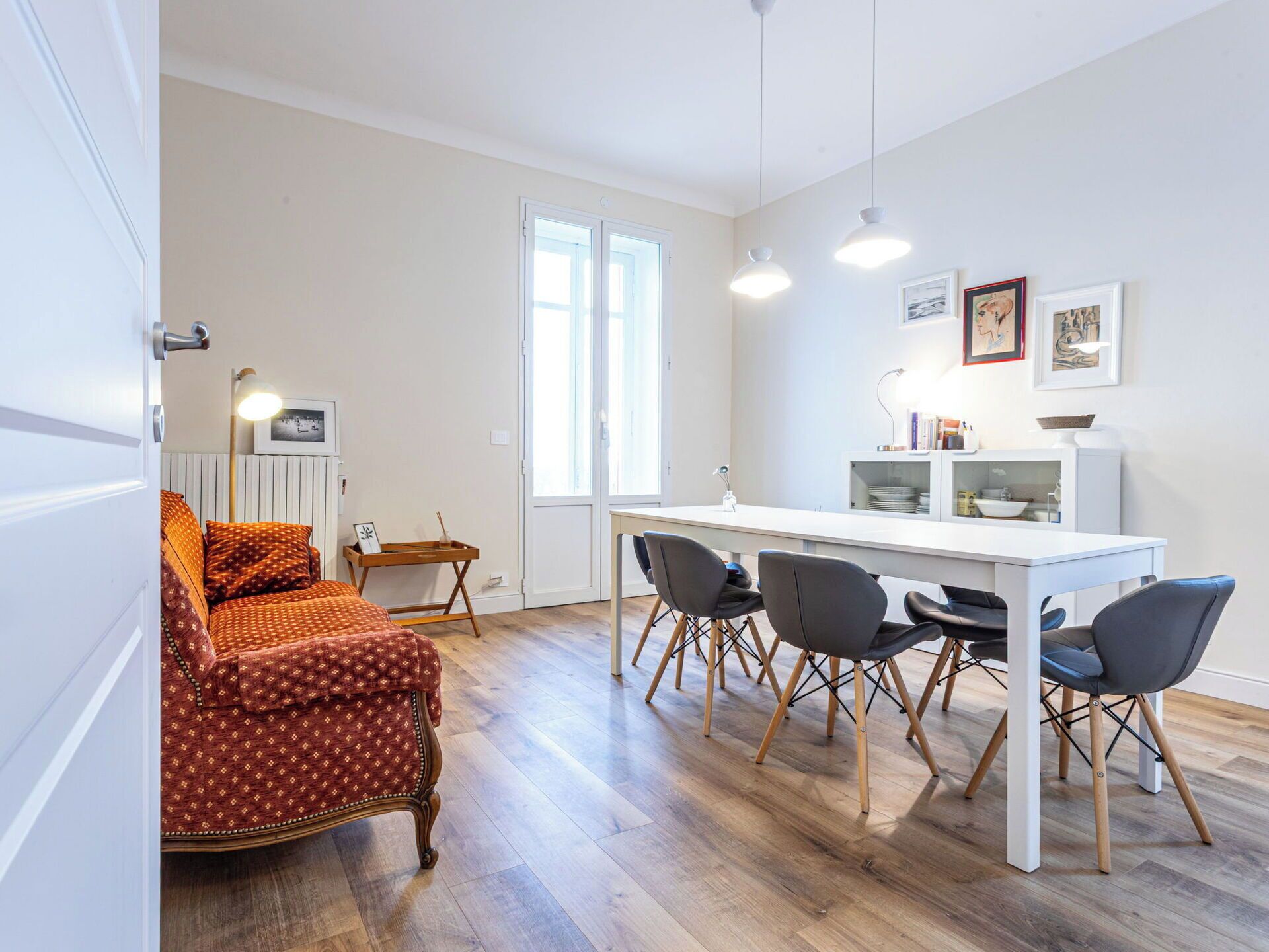 A modern living room with a sofa, dining table, chairs, and a kitchen area with a sink and cabinets.