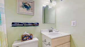 A bathroom with a toilet, a sink, a mirror, and a shelf with makeup items. - Purnell House 206 (Ocean City)