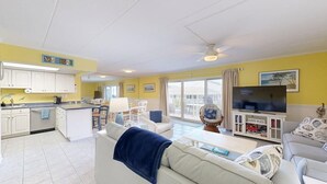 A living room with a sofa, a coffee table, a TV, and a bookshelf. - Purnell House 206 (Ocean City)