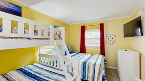 A room with bunk beds, a window with blinds, a TV, and a small cabinet. - Purnell House 206 (Ocean City)
