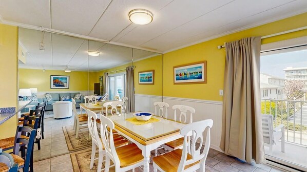 A dining area with a long table, white chairs, and a yellow wall. - Purnell House 206 (Ocean City)