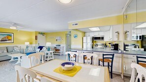 A modern kitchen with white cabinets, a central island, and a dining area with a table and chairs. - Purnell House 206 (Ocean City)