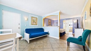 Um quarto com um sofá azul, uma poltrona verde-água, uma cama e uma mesa pequena.