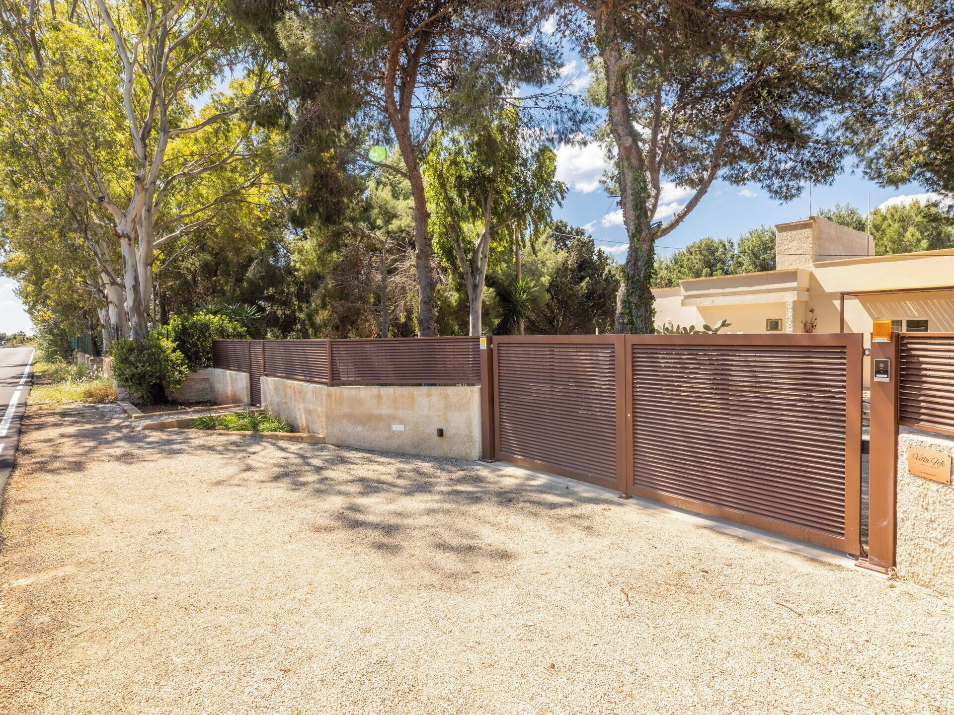 A gated property with a gravel driveway, a metal fence, and trees in the background.
