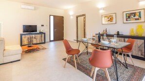 Ein modernes Wohnzimmer mit einem Glastisch, orangefarbenen Stühlen, einer Couch und einem Fernseher.