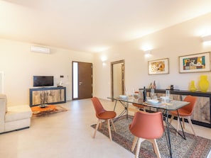 Ein modernes Wohnzimmer mit einem Glastisch, orangefarbenen Stühlen, einer Couch und einem Fernseher.