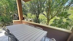 Een terras buiten met een tafel en stoelen, omringd door groen en een stenen muur.