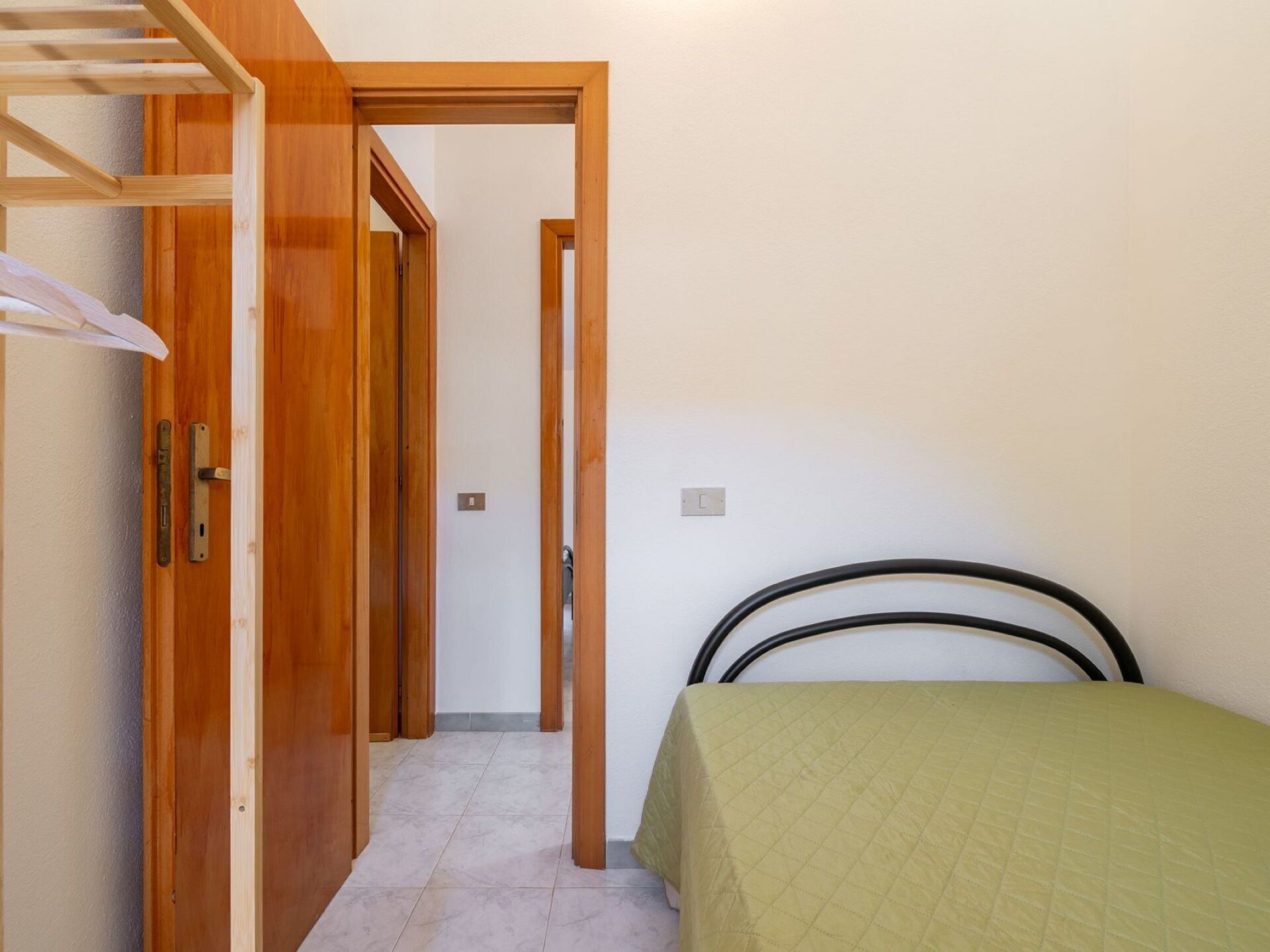 A bedroom with a bed, wooden wardrobe, and a door leading to another room.