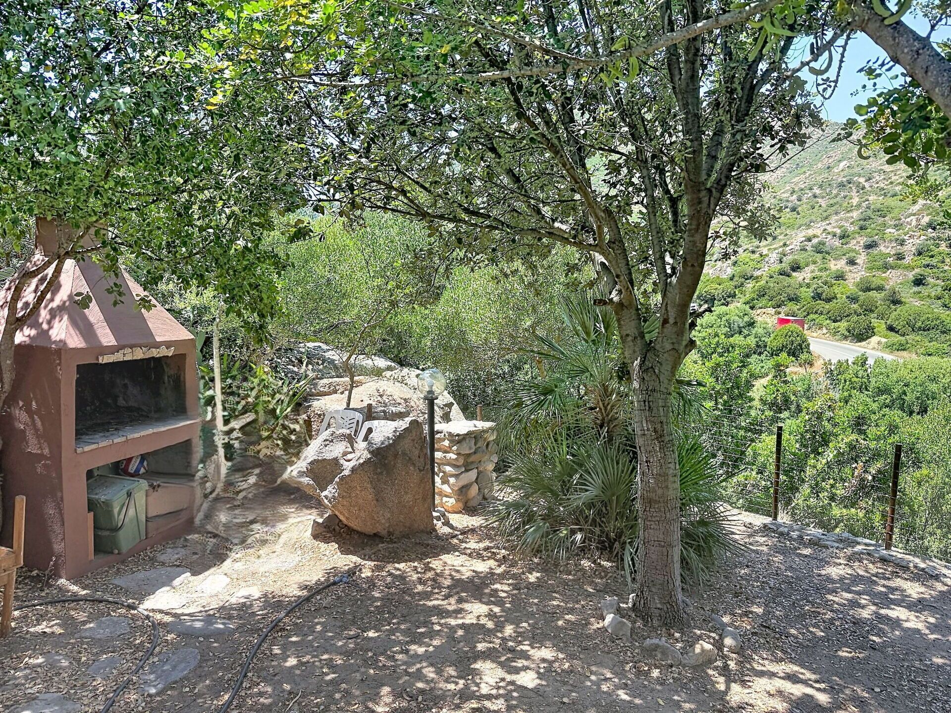 A natural outdoor setting with a small structure, possibly a shelter, and a stone wall.