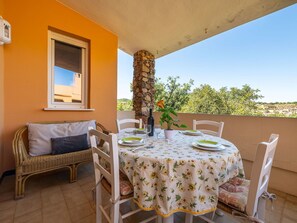 Ein Balkon mit Tisch für zwei Personen, weißen Stühlen, einer Rattan-Couch und einer Steinsäule.