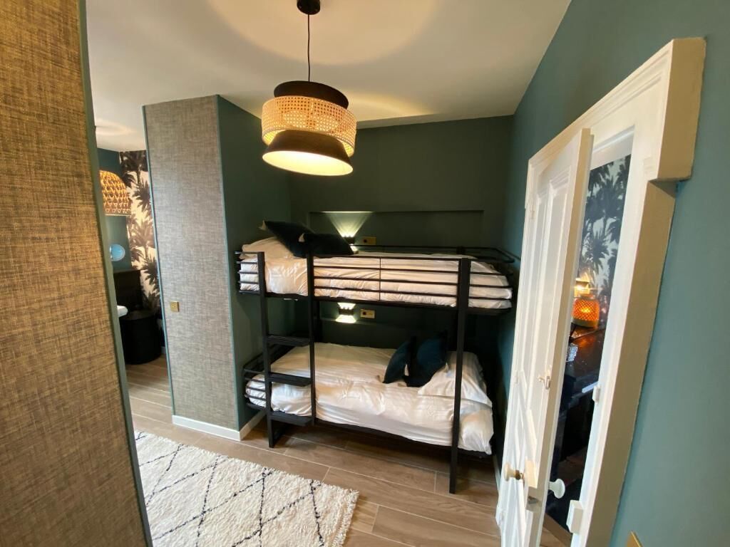 A bunk bed room with a hanging light fixture, a door with a picture frame, and a patterned rug on the floor.