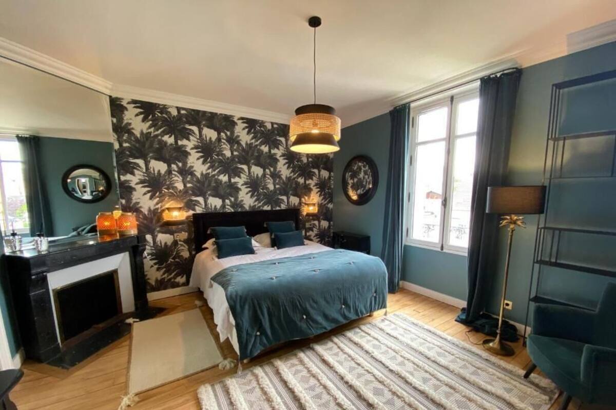 A bedroom with a bed, a fireplace, a large window, and a blue wall.
