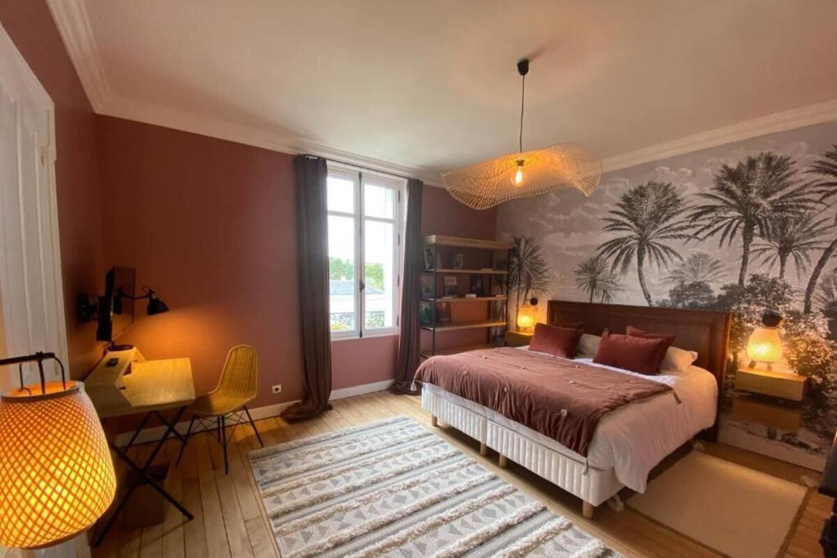 A bedroom with a bed, a desk, a chair, a lamp, and a mural on the wall.
