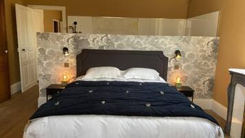 Un dormitorio con cama, mesitas de noche, espejo y lámpara de pared.
