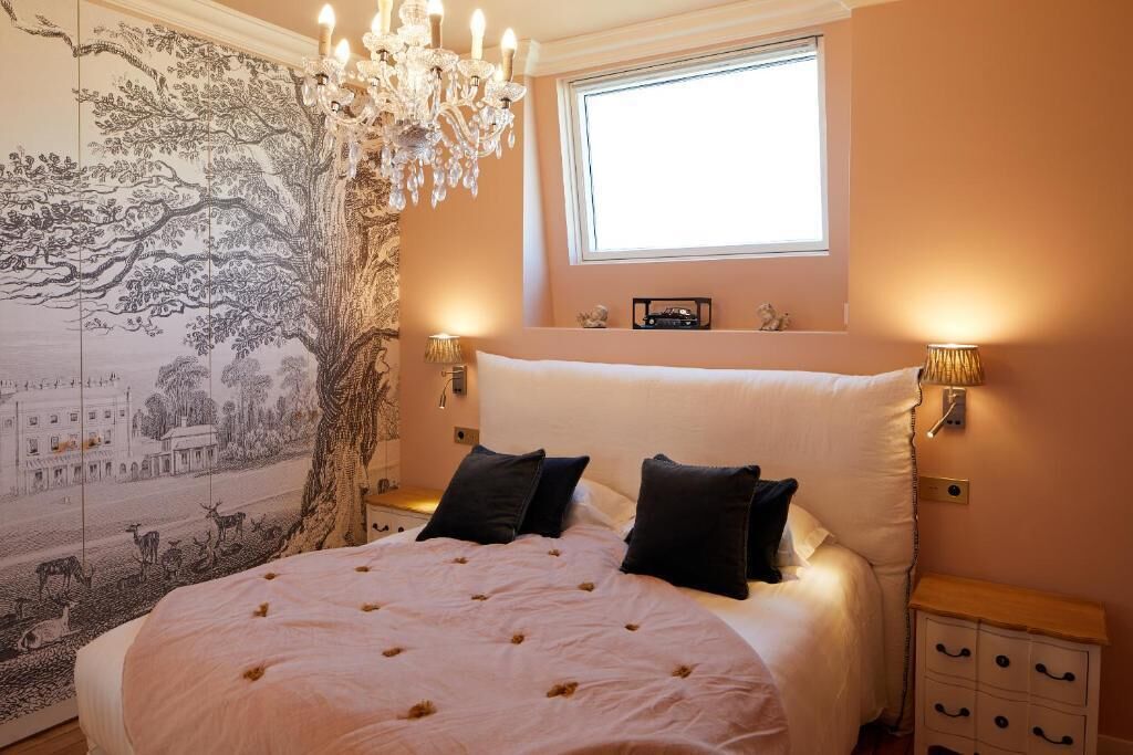 A bedroom with a large bed, a chandelier, a tapestry, and a window.
