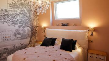 A bedroom with a large bed, a chandelier, a tapestry, and a window.