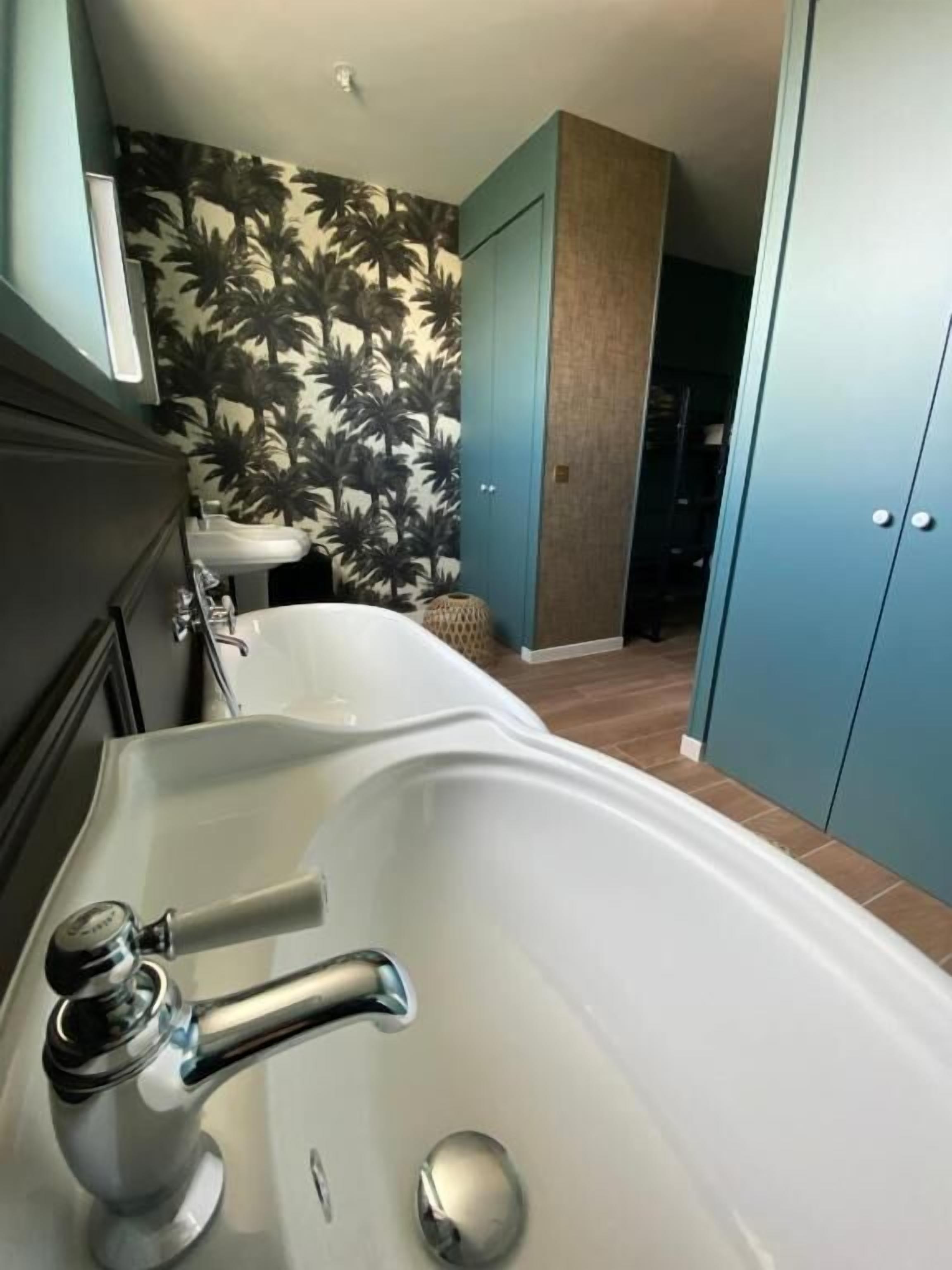 Une salle de bain avec une baignoire, un lavabo et un mur orné d’un motif de palmiers.