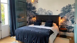 A bedroom with a bed, a hanging light fixture, a wall mural, and a window with curtains. - Villa Gabriel Maison Blanche Chartres (Chartres)