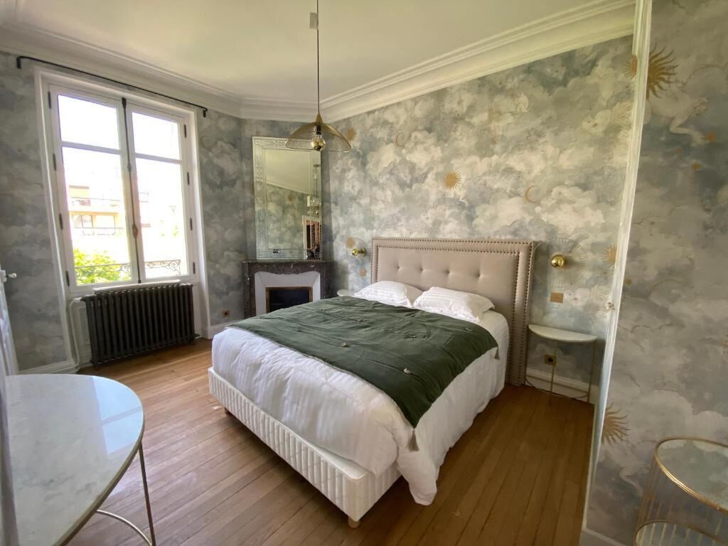 A bedroom with a bed, a round table, a radiator, a mirror, and a window.