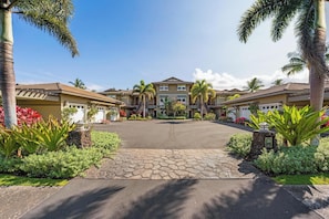 A residential complex with multiple two-story houses, a paved driveway, and landscaped gardens with tropical plants. - Halii Kai 23G | Luxury Waikoloa Villa with Exclusive Ocean Club Access (WAIKOLOA)