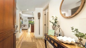 Un pasillo con una puerta de madera, una consola con un espejo, una señal decorativa y una planta en maceta.