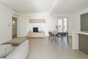 Ein modernes Wohnzimmer mit Sofa, Essbereich mit Tisch und Stühlen, Fernseher auf einer Holzkommode und einer Küchenarbeitsplatte.