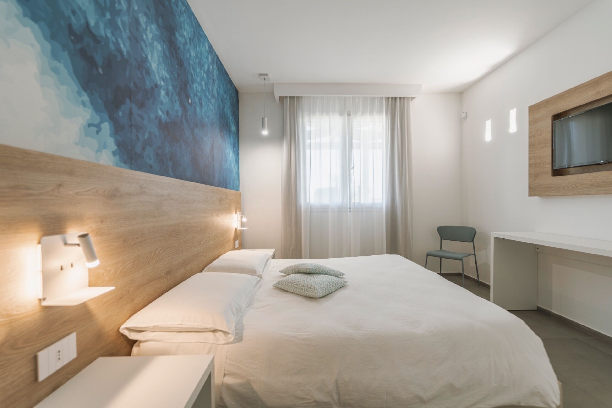 Ein Hotelzimmer mit einem großen Bett, einem Schreibtisch, einem Sessel, einem an der Wand befestigten Fernseher und einem Wandbild.