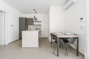 Eine moderne Küche mit einer zentralen Kochinsel, einem Essbereich mit Tisch und Stühlen sowie einer Klimaanlage an der Wand.