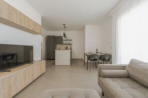 Ein modernes Wohnzimmer mit einer Couch, einem Fernseher und einem Essbereich mit Stühlen und einem Tisch.