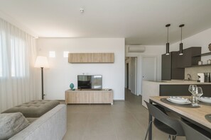 Ein modernes Wohnzimmer mit einer Couch, einem Fernseher, einer Lampe und einem Essbereich mit Tisch für zwei Personen.