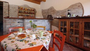 A dining area with a brick wall, wooden ceiling beams, a table with a floral tablecloth, and a cabinet with glass doors.