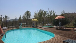 A wooden deck with a swimming pool, lounge chairs, and umbrellas.