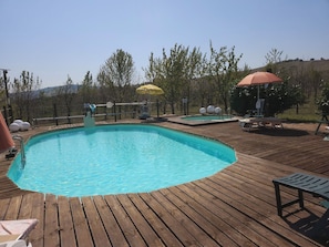 Une terrasse en bois avec une piscine, des chaises longues et des parasols.