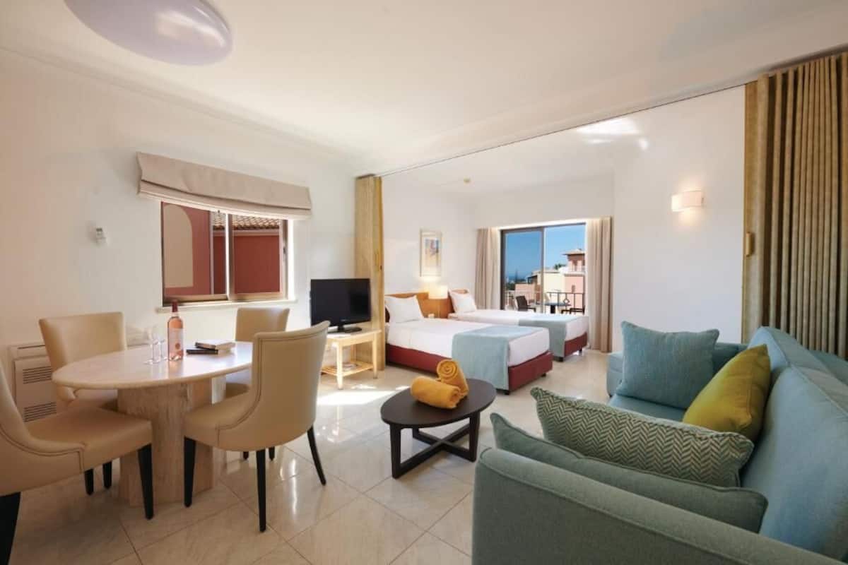 A hotel room with a dining area, a bed, a sofa, and a TV.