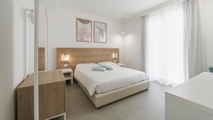 Una camera d'albergo moderna con una testiera in legno, un letto con lenzuola bianche, un comodino e una scrivania.
