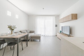 Ein modernes, minimalistisches Zimmer mit Essbereich, Sofa, Fernseher und einem großen Fenster mit durchsichtigen Vorhängen.