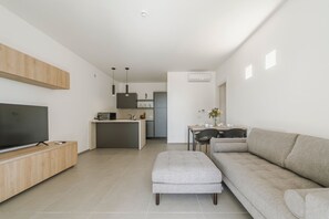 Ein modernes Wohnzimmer mit Flachbildfernseher, grauem Sofa und kleinem Hocker.