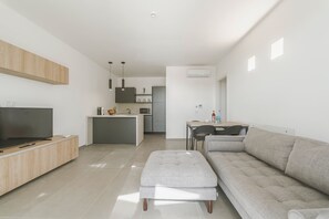 A modern living room with a flat-screen TV, a grey sofa, and a small ottoman. - Venti di Laguna Apartments Stagnone - Ponente (Marsala)
