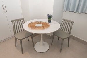 Una mesa redonda con un centro de mesa tejido, dos sillas, una pequeña planta en maceta y un armario blanco.