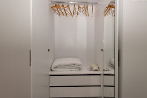 A white wardrobe with a mirror, a folded white blanket, and a pair of slippers. - Modern Seaside Escape Steps From Gytheio Harbor (East Mani)