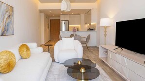 Una sala de estar moderna con un sofá, una mesa de centro, un televisor y una cocina al fondo.