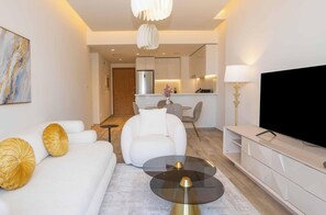 Ein modernes Wohnzimmer mit einer Couch, einem Couchtisch, einem Fernseher und einer Küchenzeile im Hintergrund.