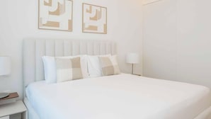 Un cuarto de hotel ordenado, con una cama grande, una mesita de noche, una lámpara y dos obras de arte abstracto en la pared.