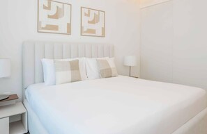 Ein ordentlich eingerichtetes Hotelzimmer mit einem großen Bett, einem Nachttisch, einer Lampe und zwei abstrakten Wandbildern.