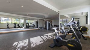 Un gimnasio con máquinas de cardio, equipo de entrenamiento con pesas y ventanas amplias.