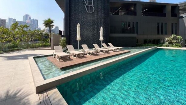 Un hotel moderno con piscina en la azotea, sillas de descanso y vistas a un horizonte urbano.