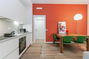 Eine moderne Küche mit weißen Schränken, ein Essbereich mit einem Holztisch und grünen Stühlen sowie eine rote Akzentwand.