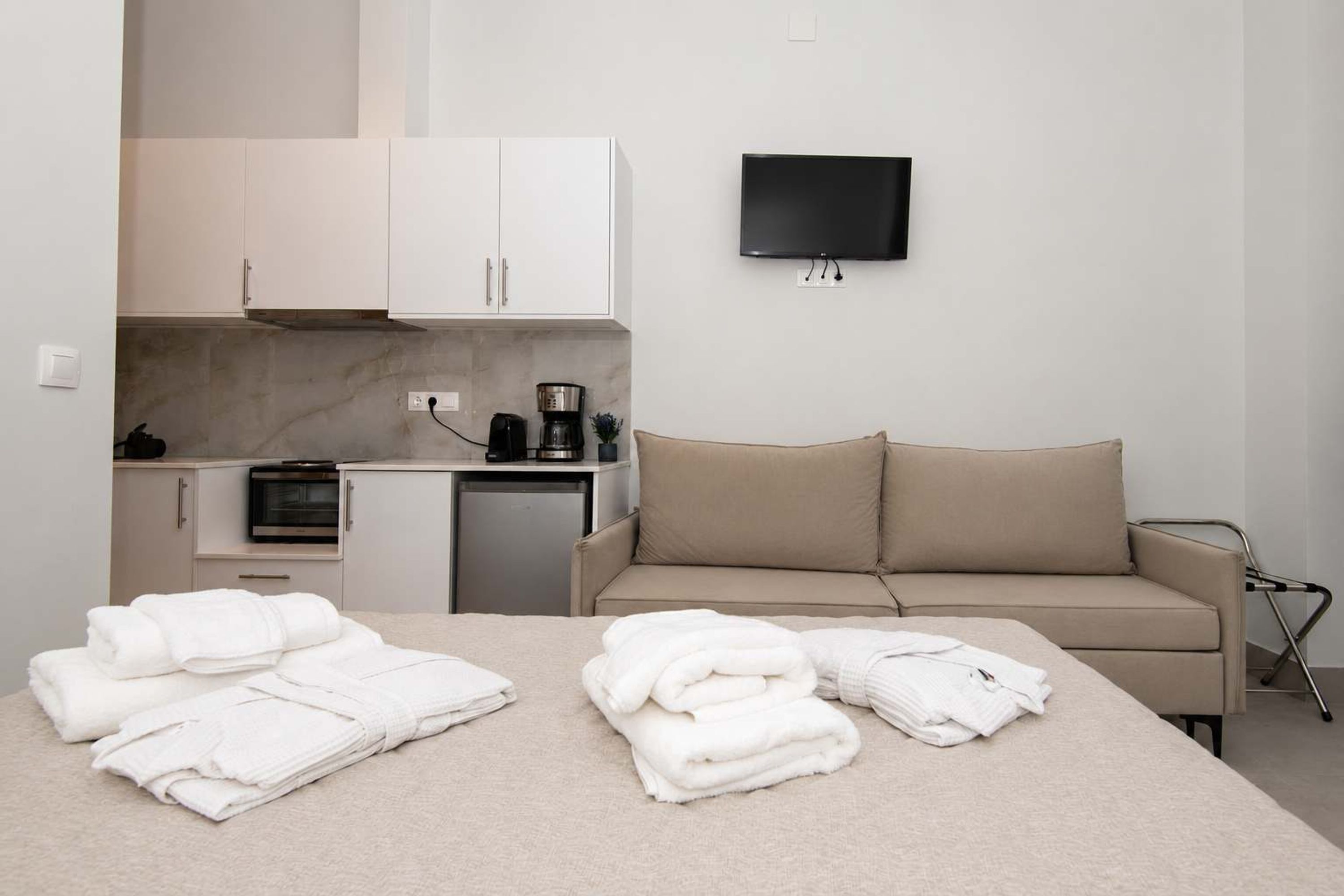 Quarto de hotel com cama, sofá, televisão, cozinha compacta e banheiro.