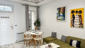 Un salon avec un canapé vert, une table de salle à manger ronde entourée de chaises, une table basse, un tableau et une porte avec une fenêtre.