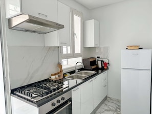Una cocina moderna con armarios blancos, estufa de acero inoxidable, horno empotrado, lavaplatos y refrigerador blanco.